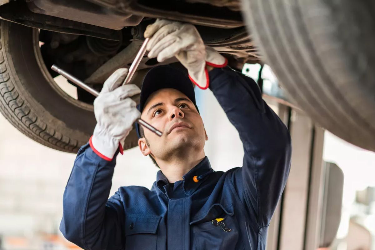 A man is working under a car with a wrench - Walt's Auto & Electric