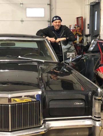 A man is standing next to a black car in a garage - Walt's Auto & Electric