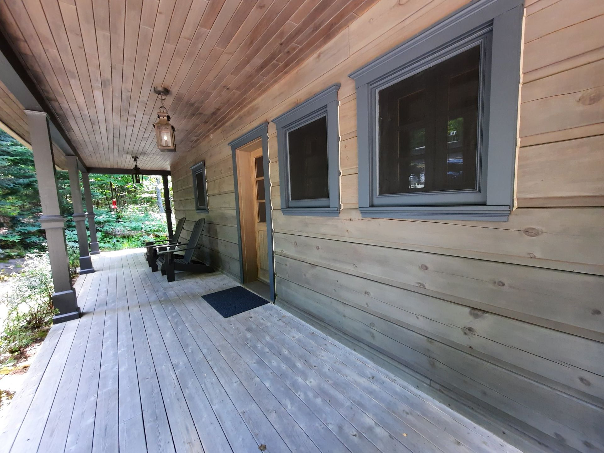 Porche d'une cabane en bois avec garniture gris-bleu autour des fenêtres, de la porte et du plafond ; deux chaises sont assises près de l'entrée.