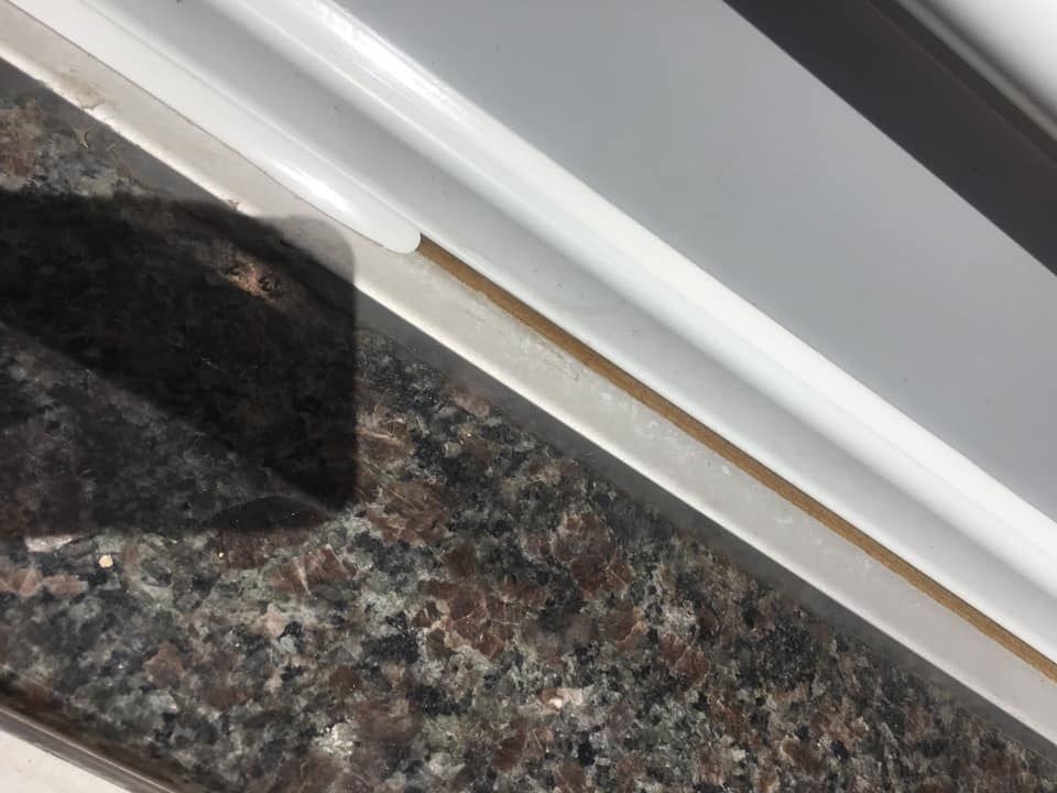 Cadre de fenêtre blanc avec une bande marron de couleur beige contre un comptoir marron moucheté.