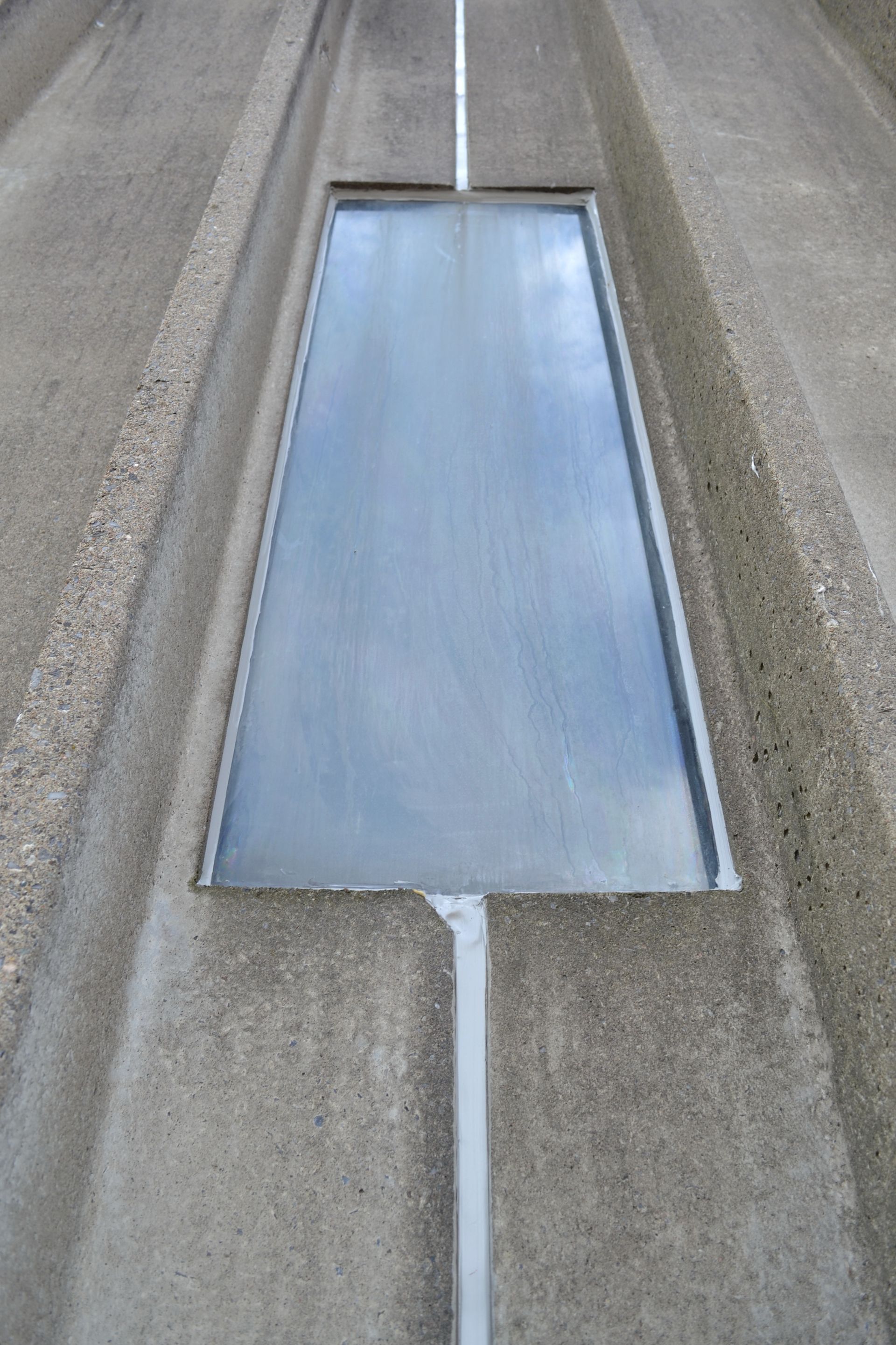 Gros plan d'un mur de bâtiment en béton avec une fenêtre rectangulaire réfléchissante placée entre des rainures verticales.