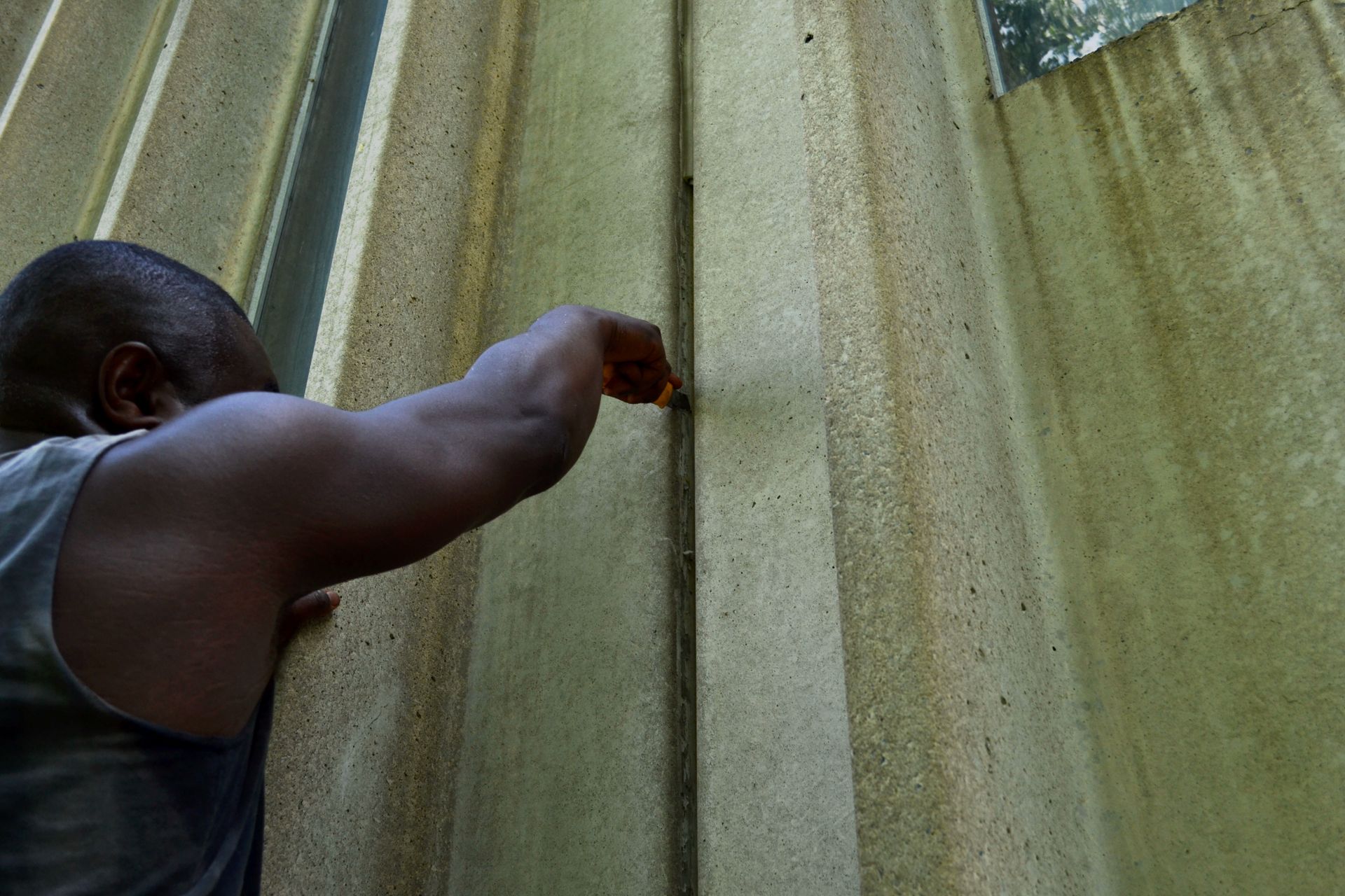 Un homme touche un mur vertical recouvert d’algues et de taches d’eau.