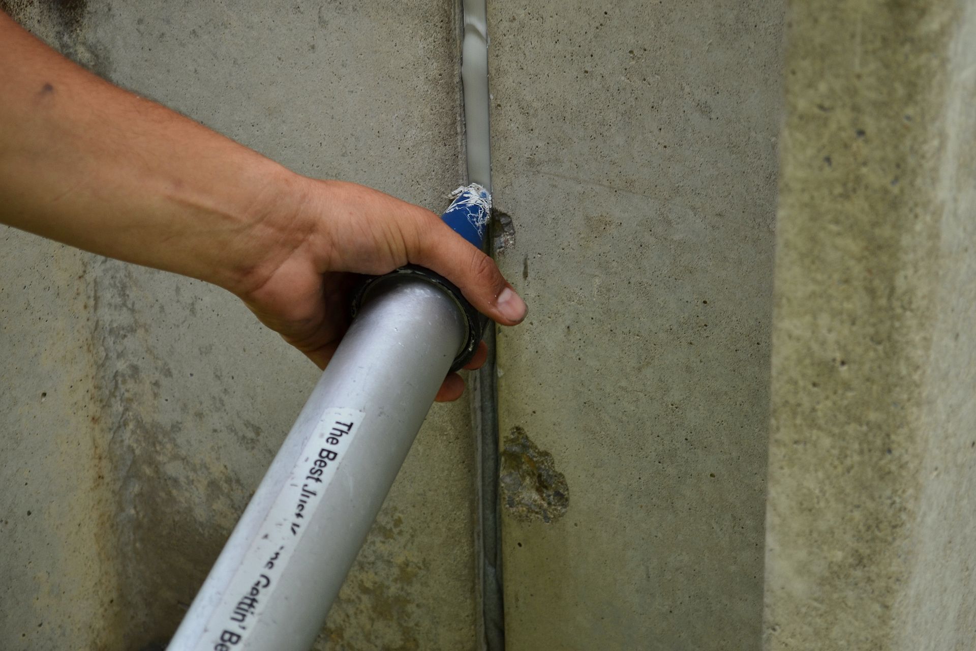 Une personne applique du mastic sur une fissure de béton avec un pistolet à calfeutrer à l'extérieur.