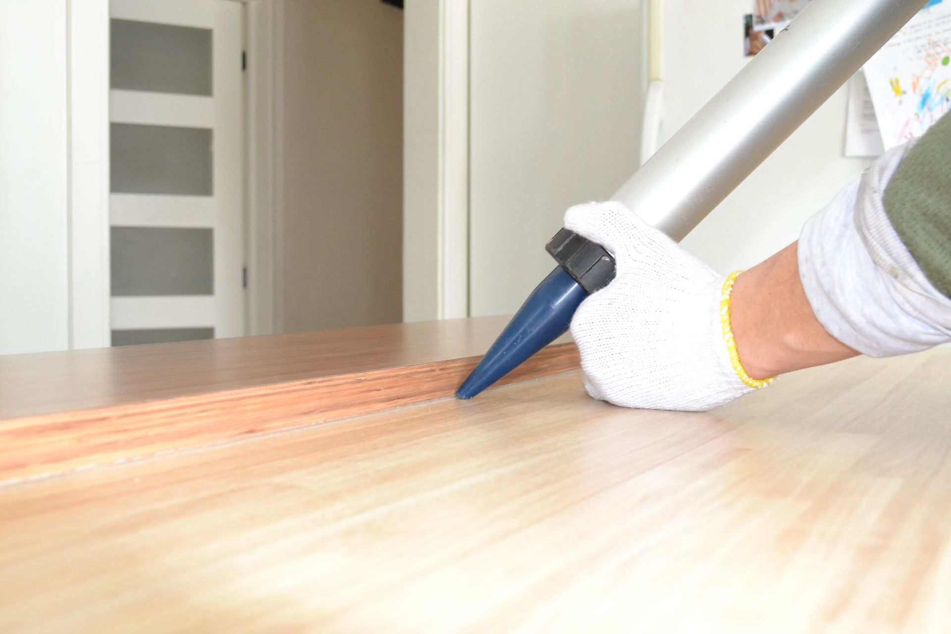 Personne portant des gants appliquant du mastic sur une surface en bois avec un pistolet à calfeutrer.