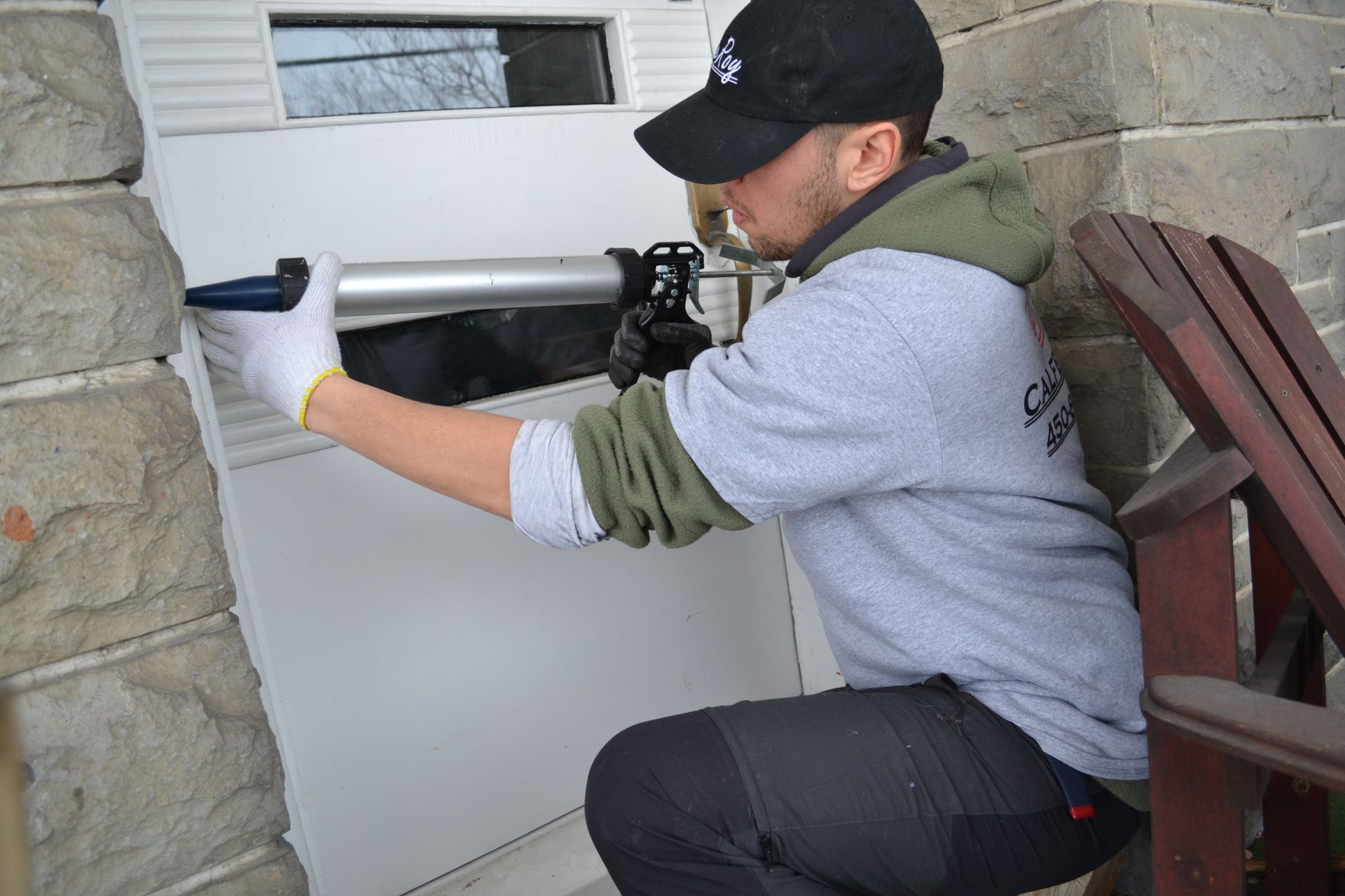Un homme portant une casquette de baseball calfeutrant le cadre d'une porte, portant des gants et agenouillé à l'extérieur.