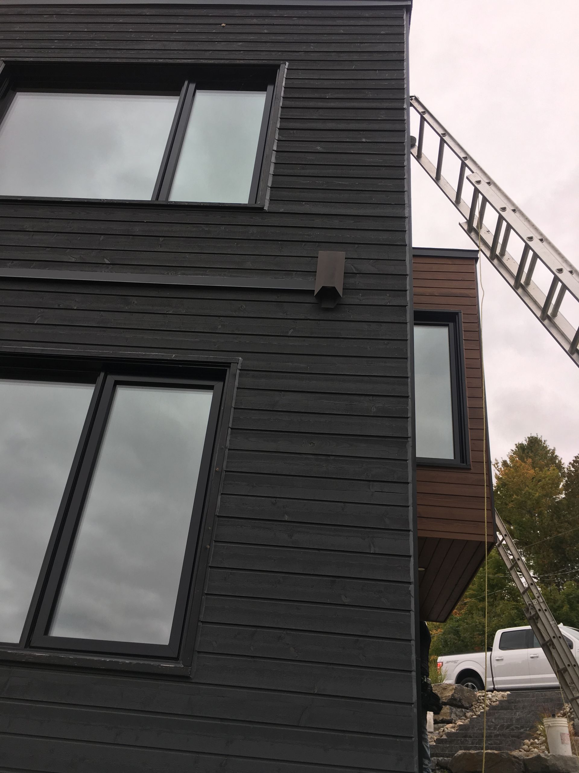 Bâtiment moderne aux murs noirs, avec des fenêtres aux cadres sombres. Une échelle est appuyée contre le mur.