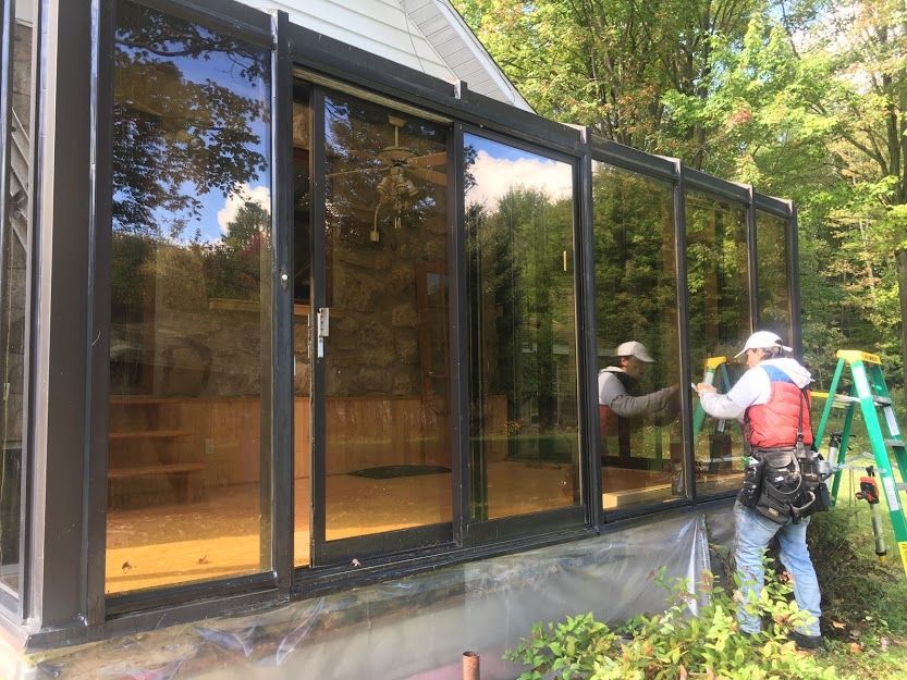 Ouvriers installant des panneaux de verre sur une véranda avec des fenêtres teintées réfléchissantes; à l'extérieur dans une zone boisée.