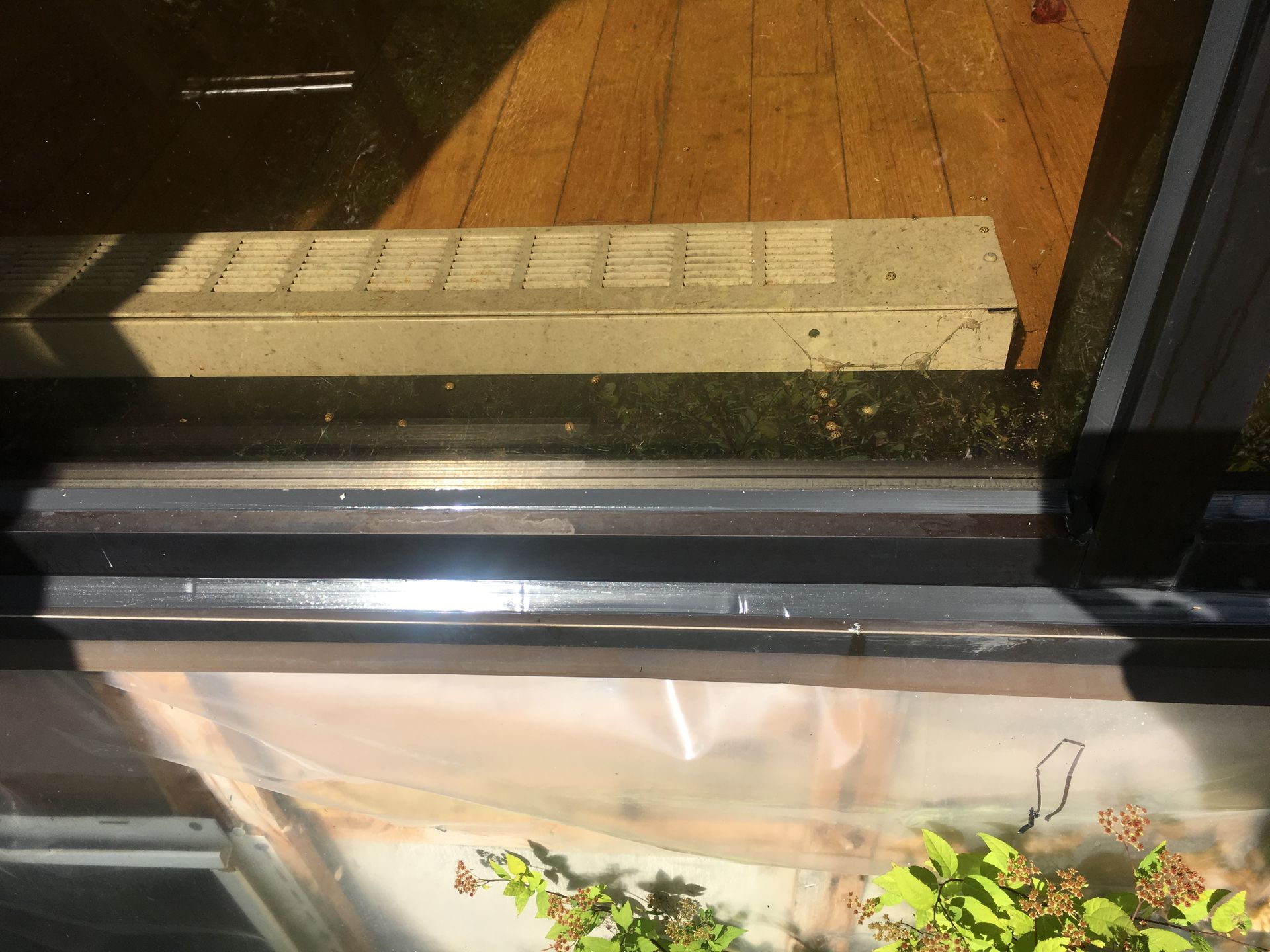 Porte coulissante en verre, montrant un rail avec des débris et un seuil en béton encastré. Plancher en bois visible.