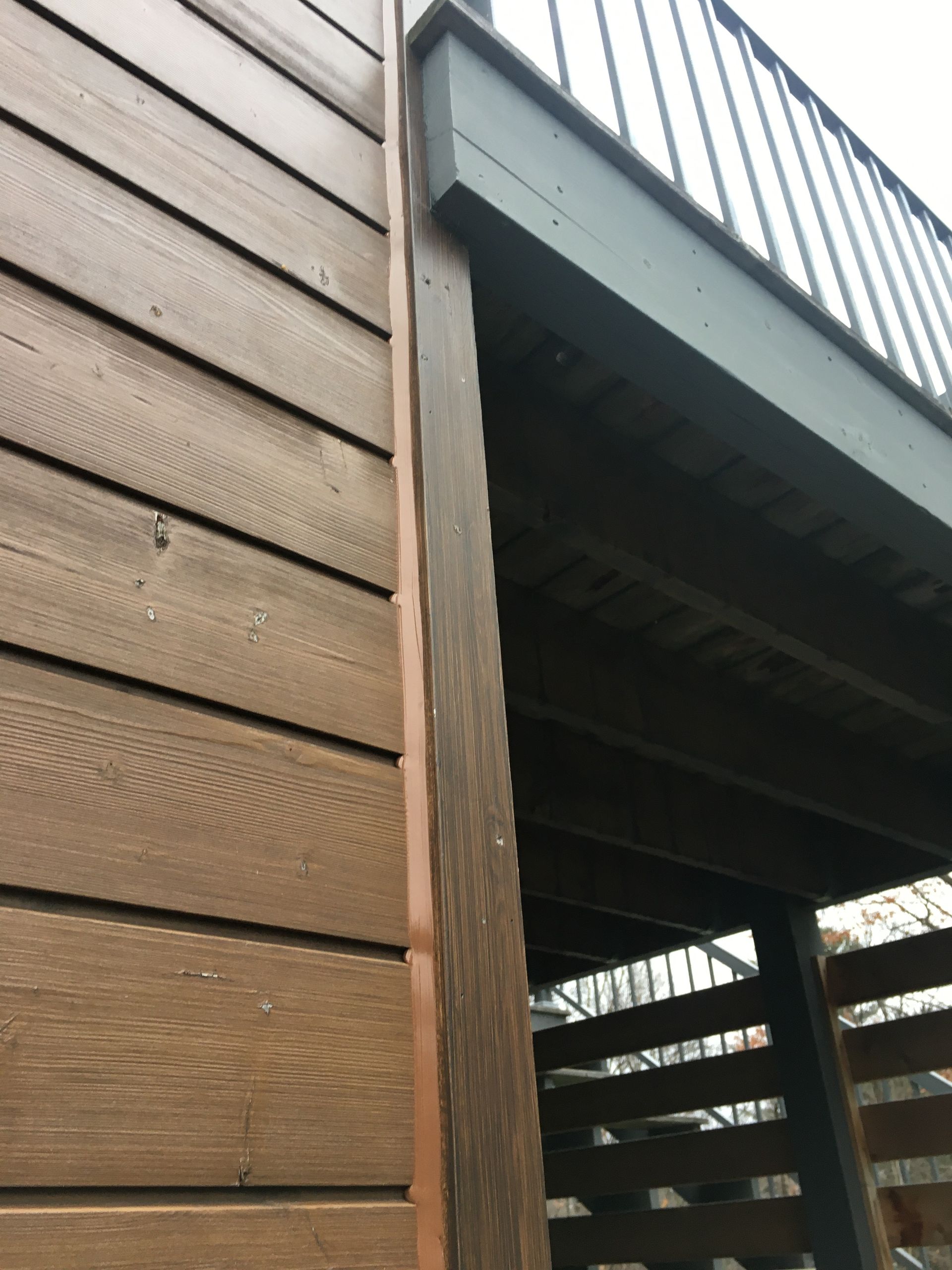 Revêtement en bois et poteau de support de terrasse. Planches et garde-corps marron foncé, éclairage tamisé.