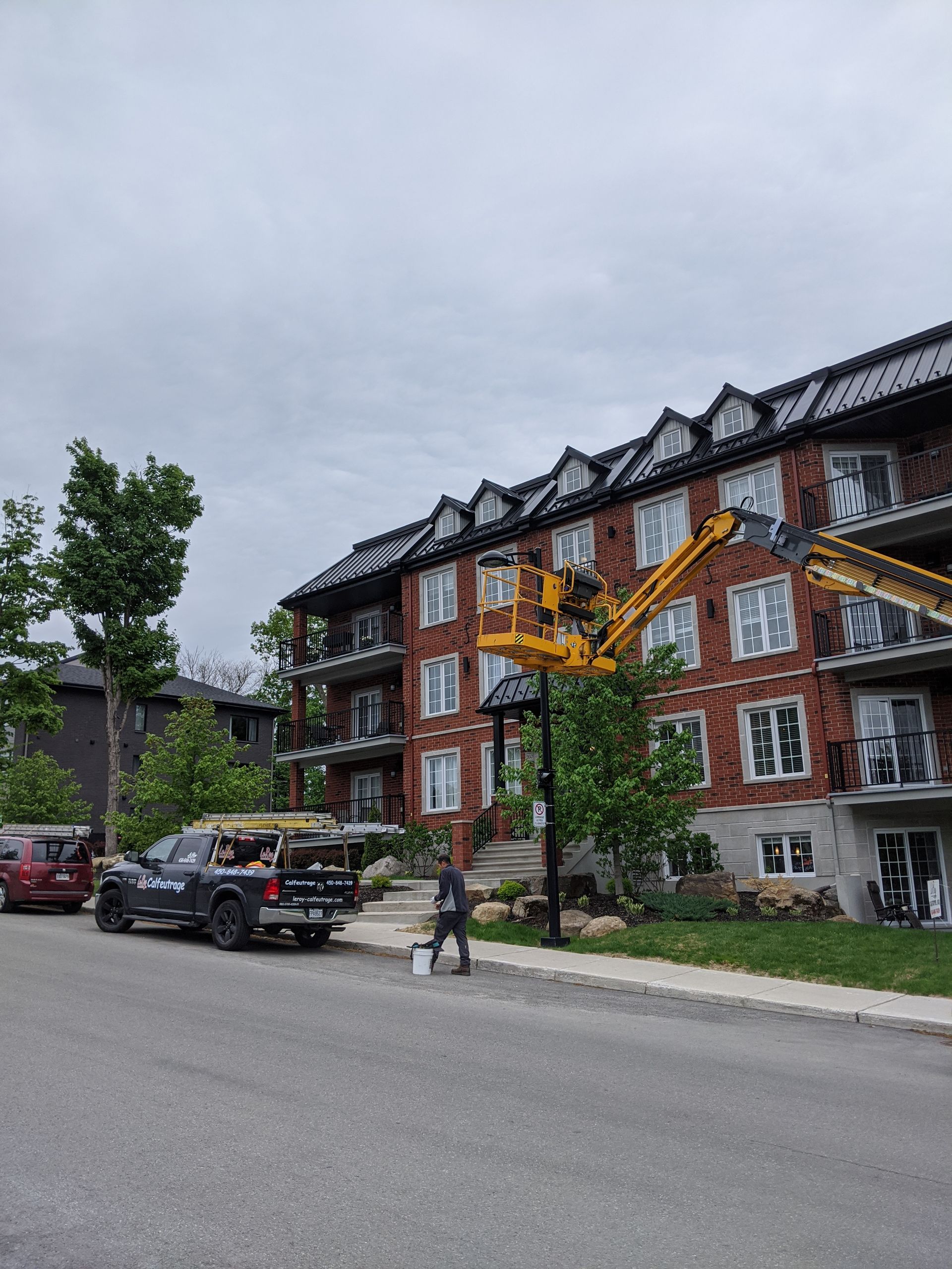 Une personne peint la façade en briques d'un immeuble d'appartements, aidée par un ascenseur jaune, par une journée nuageuse.