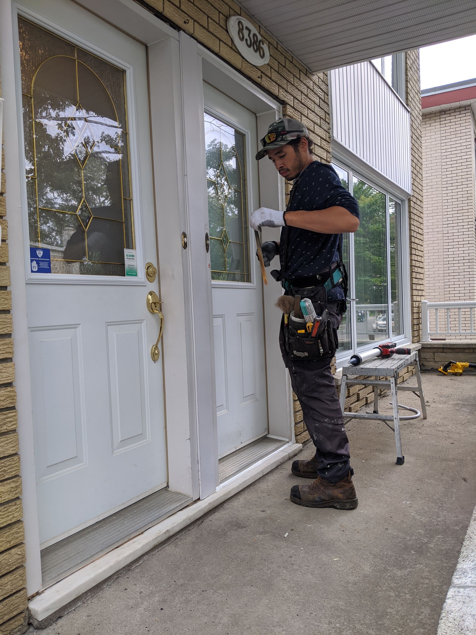 Un homme en vêtements de travail installe une garniture de porte sur l'extérieur d'un bâtiment.