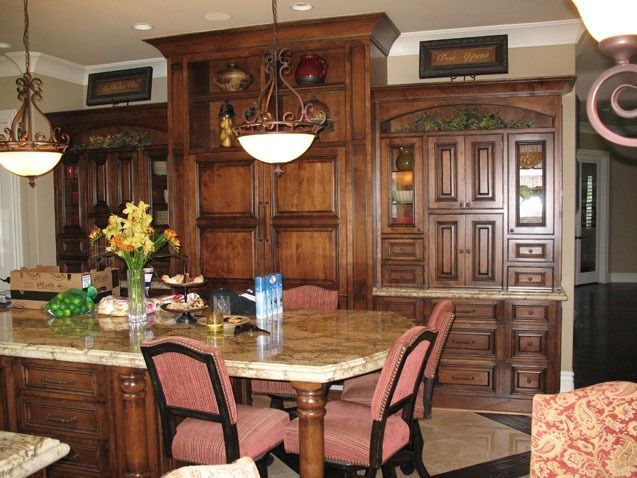 Luxurious kitchen with wood cabinets, granite island, and pink upholstered chairs