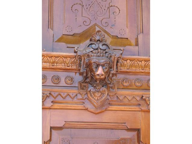 Ornate carved wooden panel with a decorative lion head centerpiece and gold trim