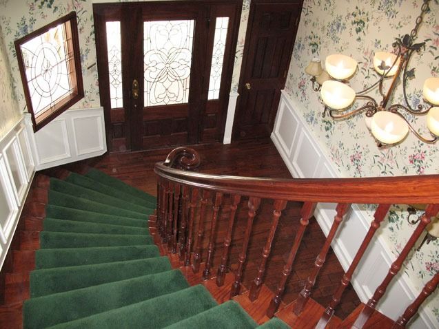 Curved staircase with red carpet, wooden banister, stained glass windows, and chandelier in an elegant foyer