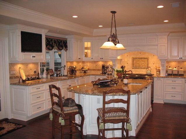 Elegant white kitchen with a large island, wood floors, and warm pendant lighting