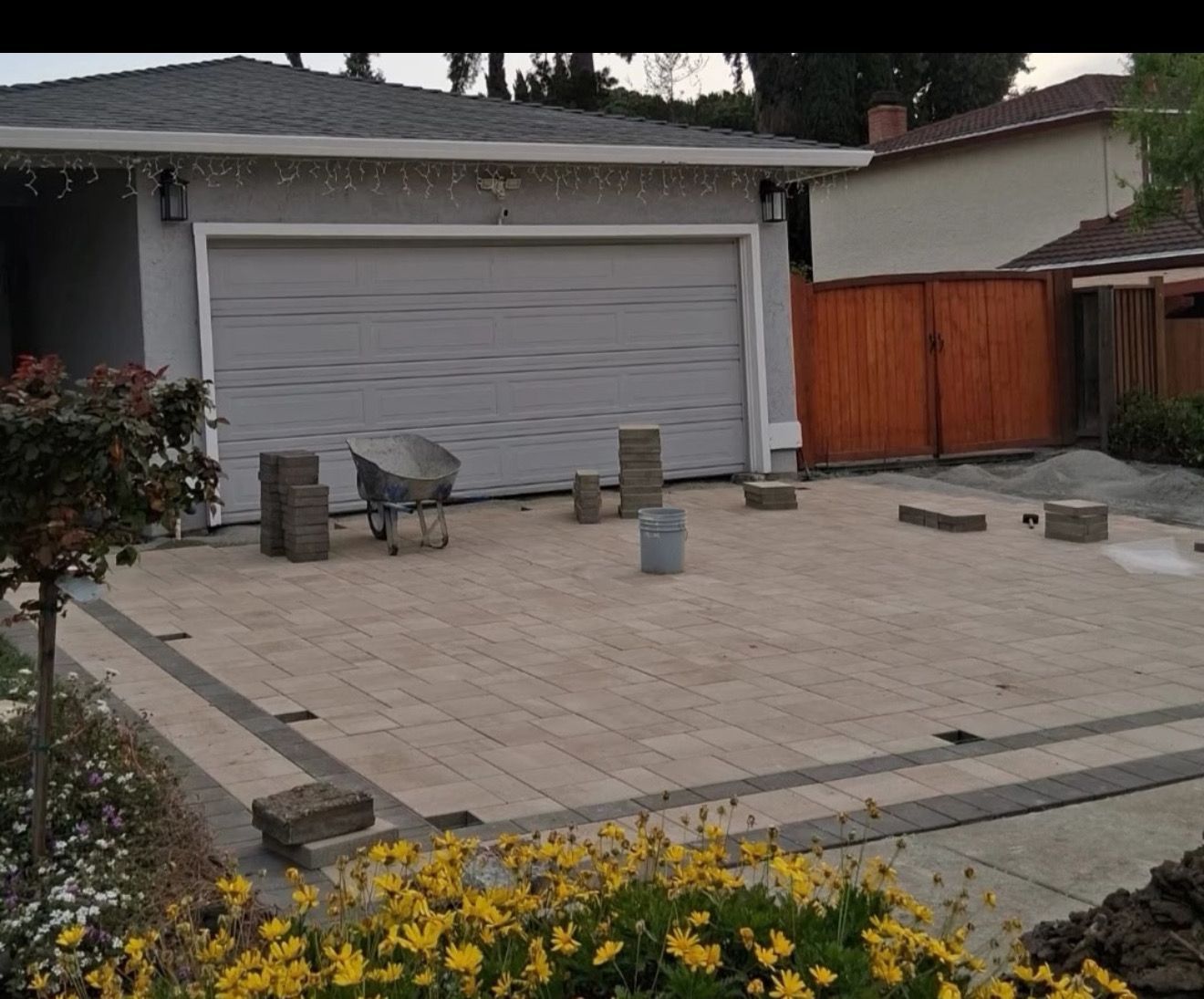 Driveway paved with tan and dark grey bricks, unfinished construction.