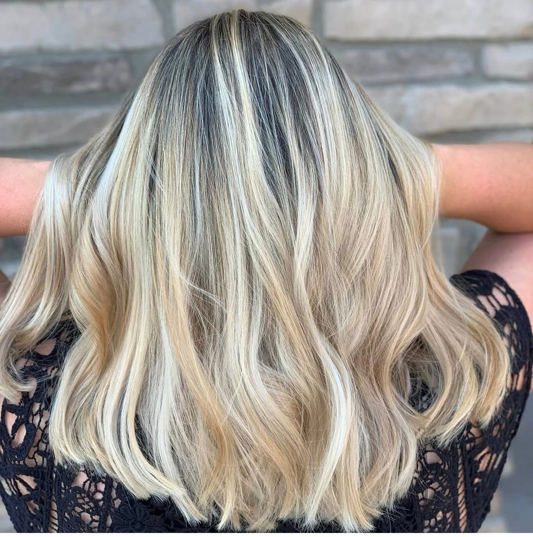 Blonde wavy hair with dark roots against a neutral background, person's back shown.