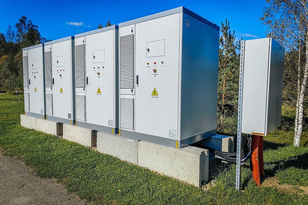 Outdoor electrical infrastructure cabinets on a concrete foundation in a grassy area with trees under a blue sky.