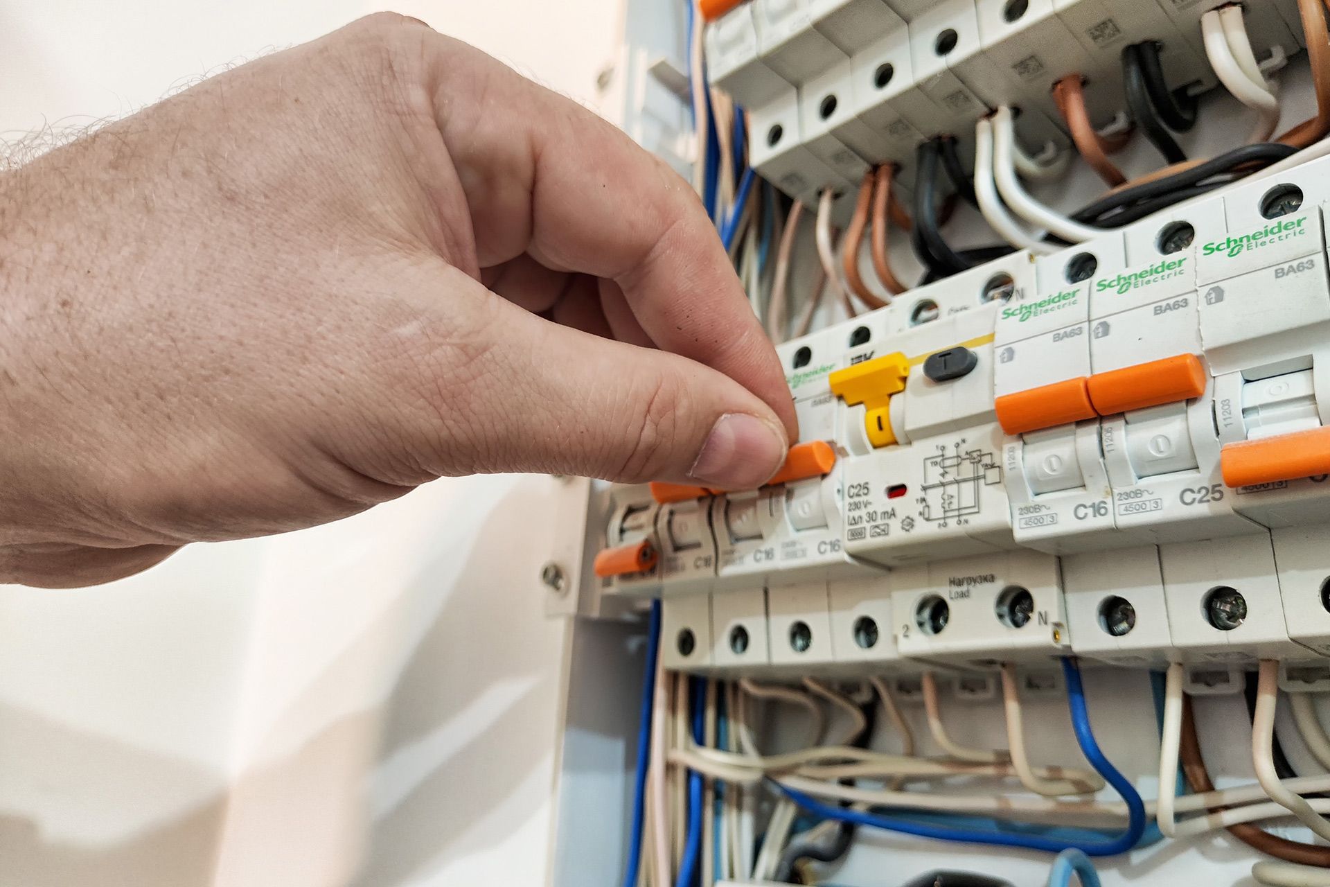 A hand flipping an orange toggle switch on an electrical distribution board filled with circuit breakers.
