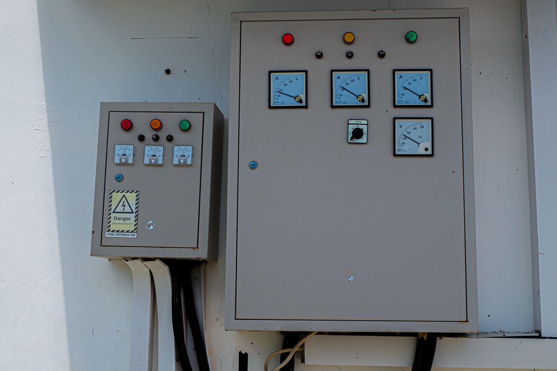 Two electrical control boxes with meters, indicator lights, and switches mounted on a white wall.