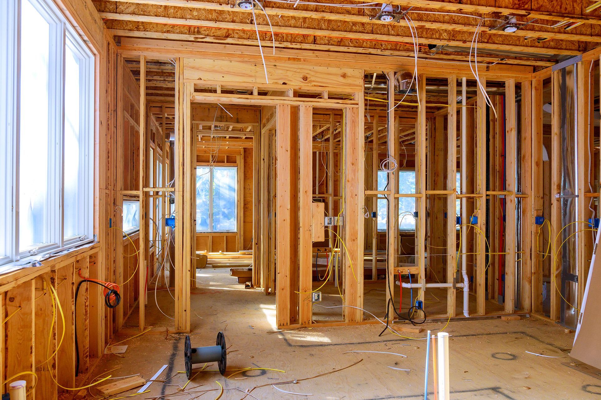 An interior view of a house under construction showing wooden wall framing, exposed wiring, and large windows.