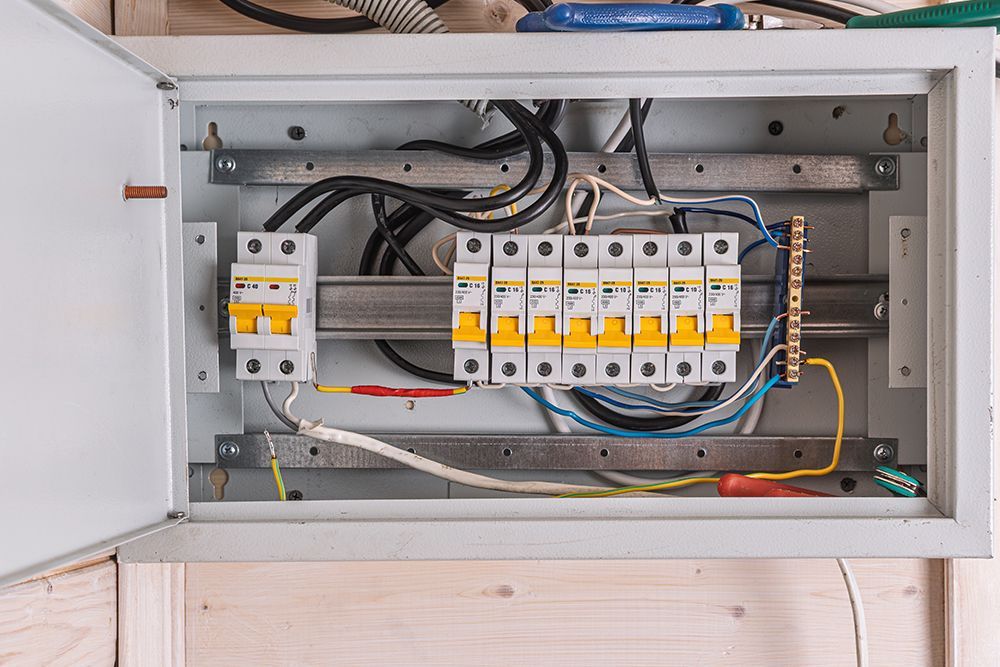 An open electrical distribution board mounted on a wooden wall, containing a main circuit breaker and several sub-breakers.