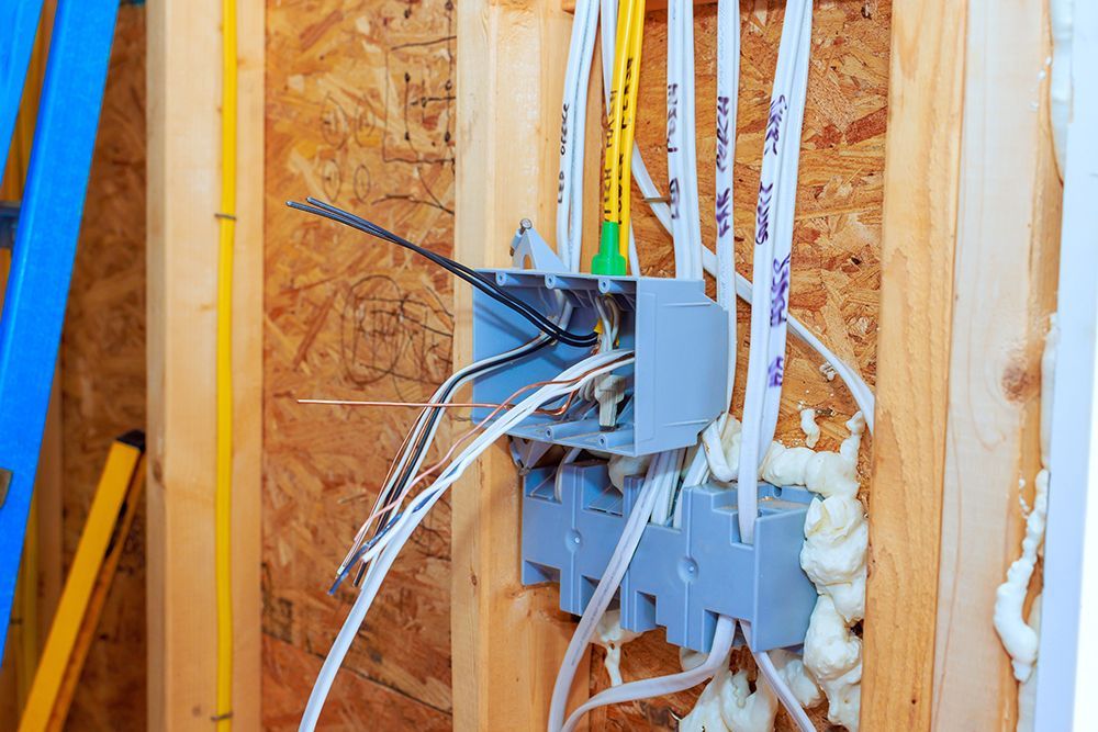 Electrical boxes mounted to wooden wall studs with multiple white and yellow electrical cables passing through them.