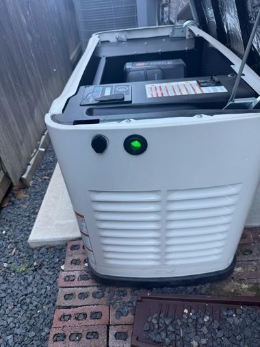 White outdoor generator next to a wooden fence, with a glowing green indicator light.
