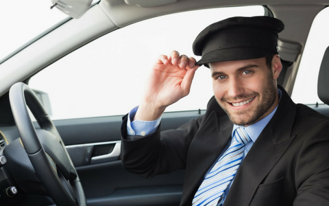 Smiling driver in a car, adjusting a black cap and wearing a suit and striped tie.