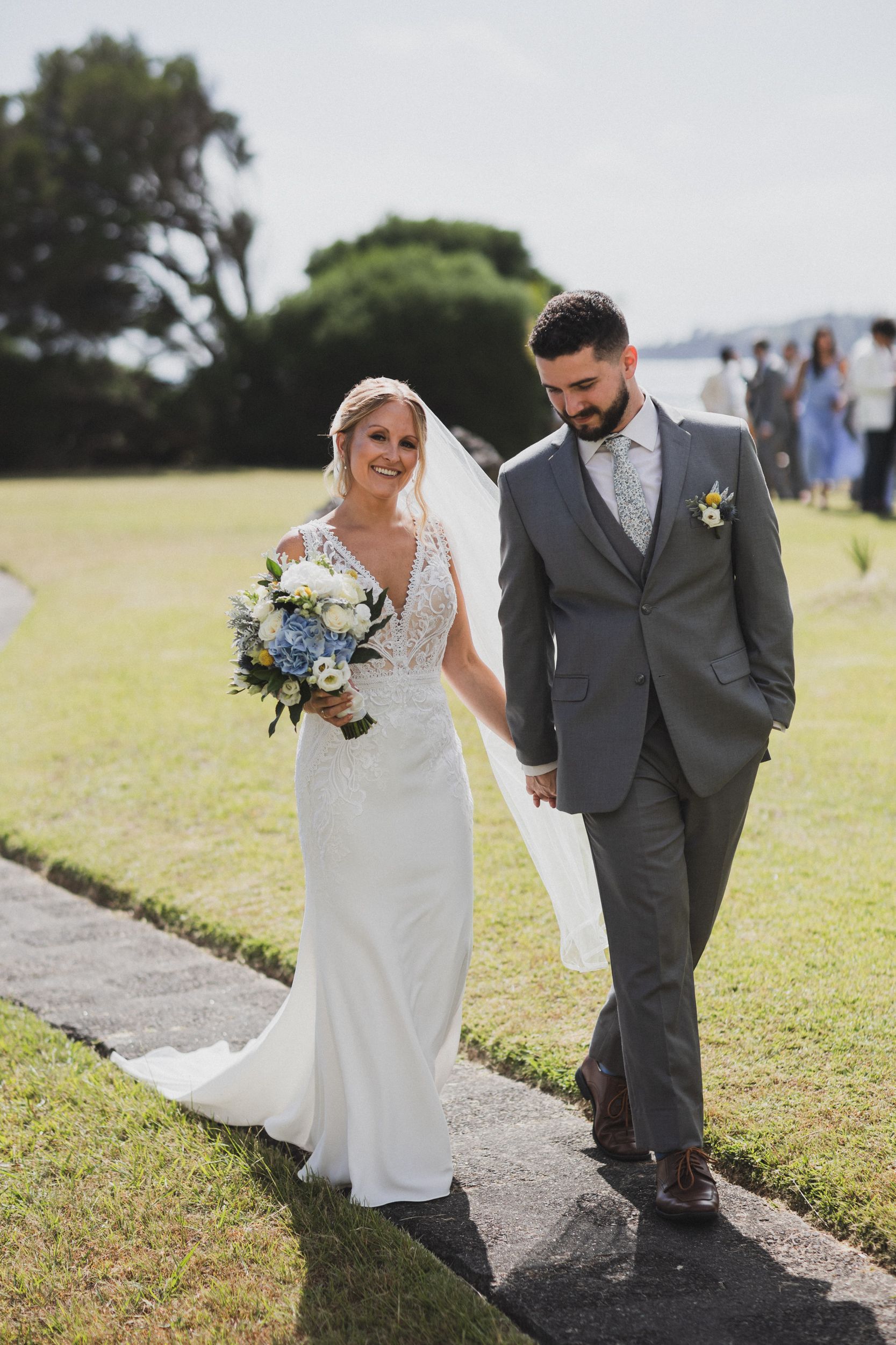 A bride and groom are walking down a path holding hands.