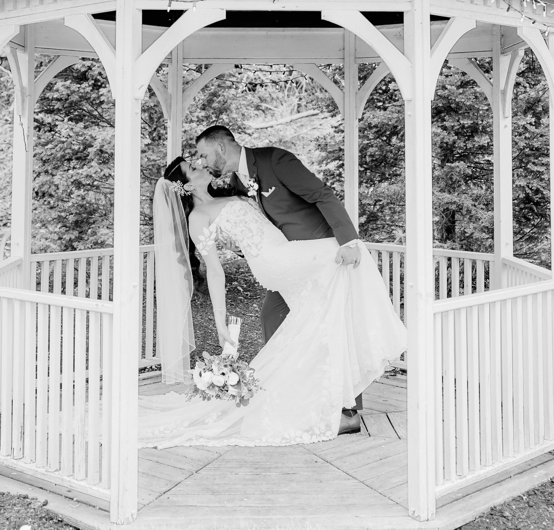 A bride and groom are kissing in a gazebo.
