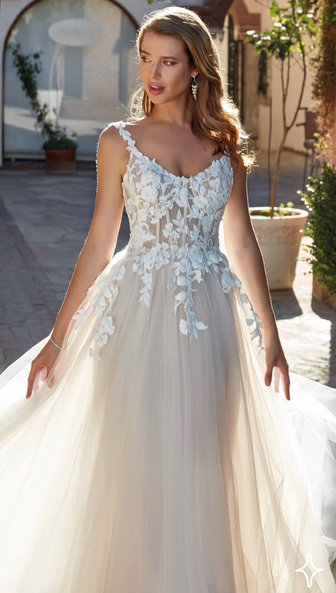 Woman in a white floral lace gown standing outdoors in sunlight.
