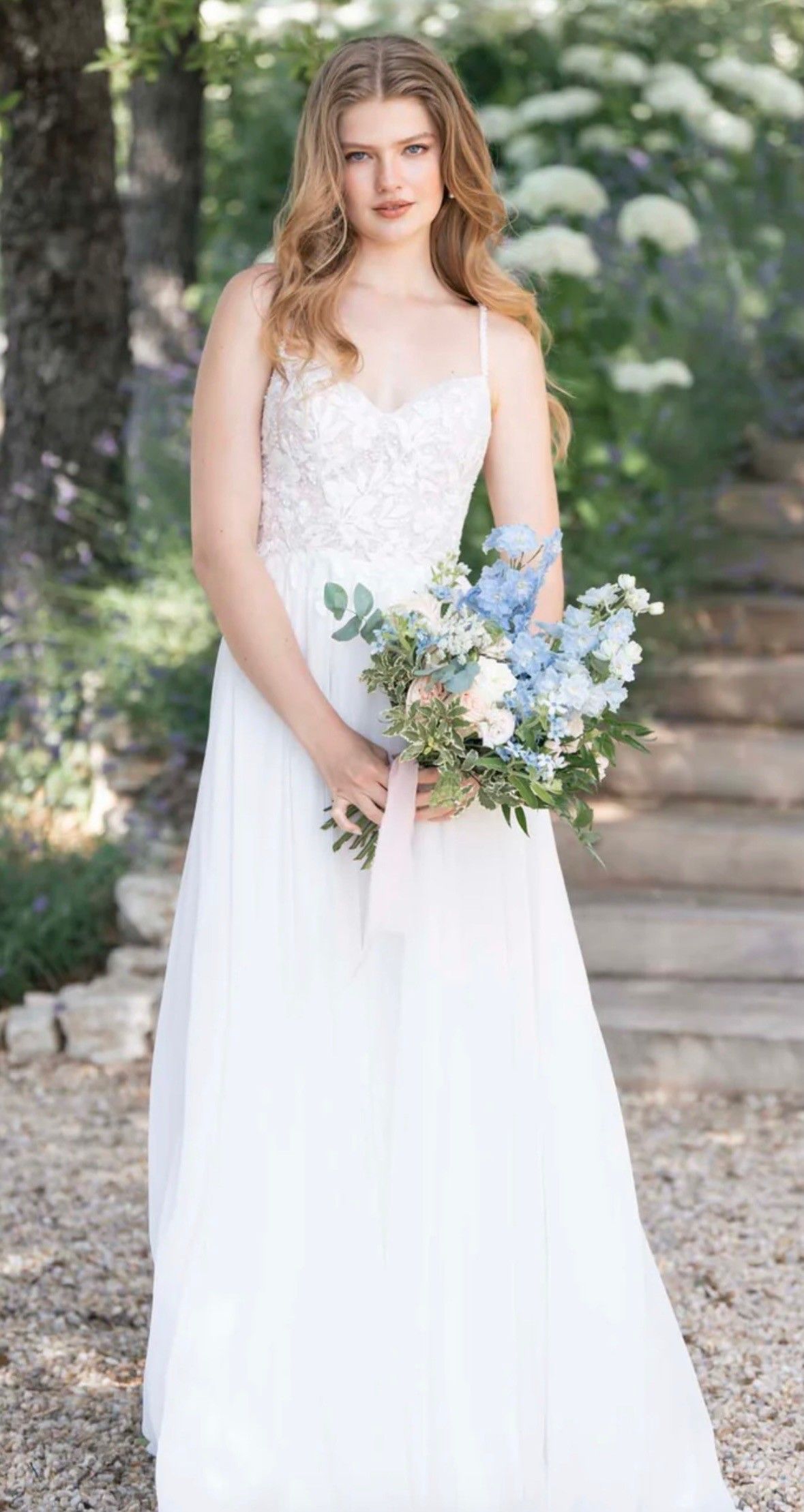 Bride in a white lace dress holding a pastel bouquet outdoors near stone steps