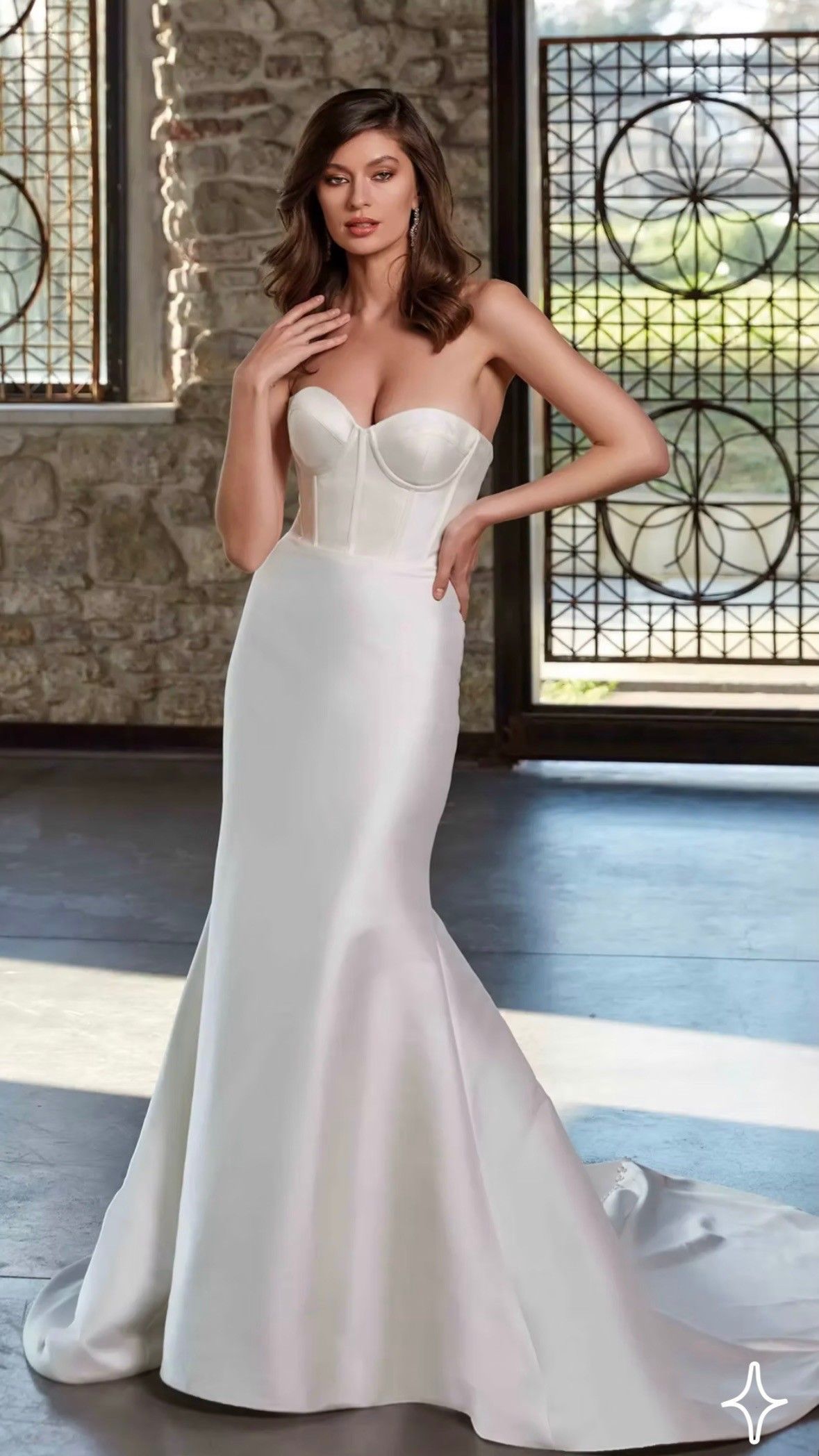 Woman in a white strapless mermaid gown posing indoors by large windows.
