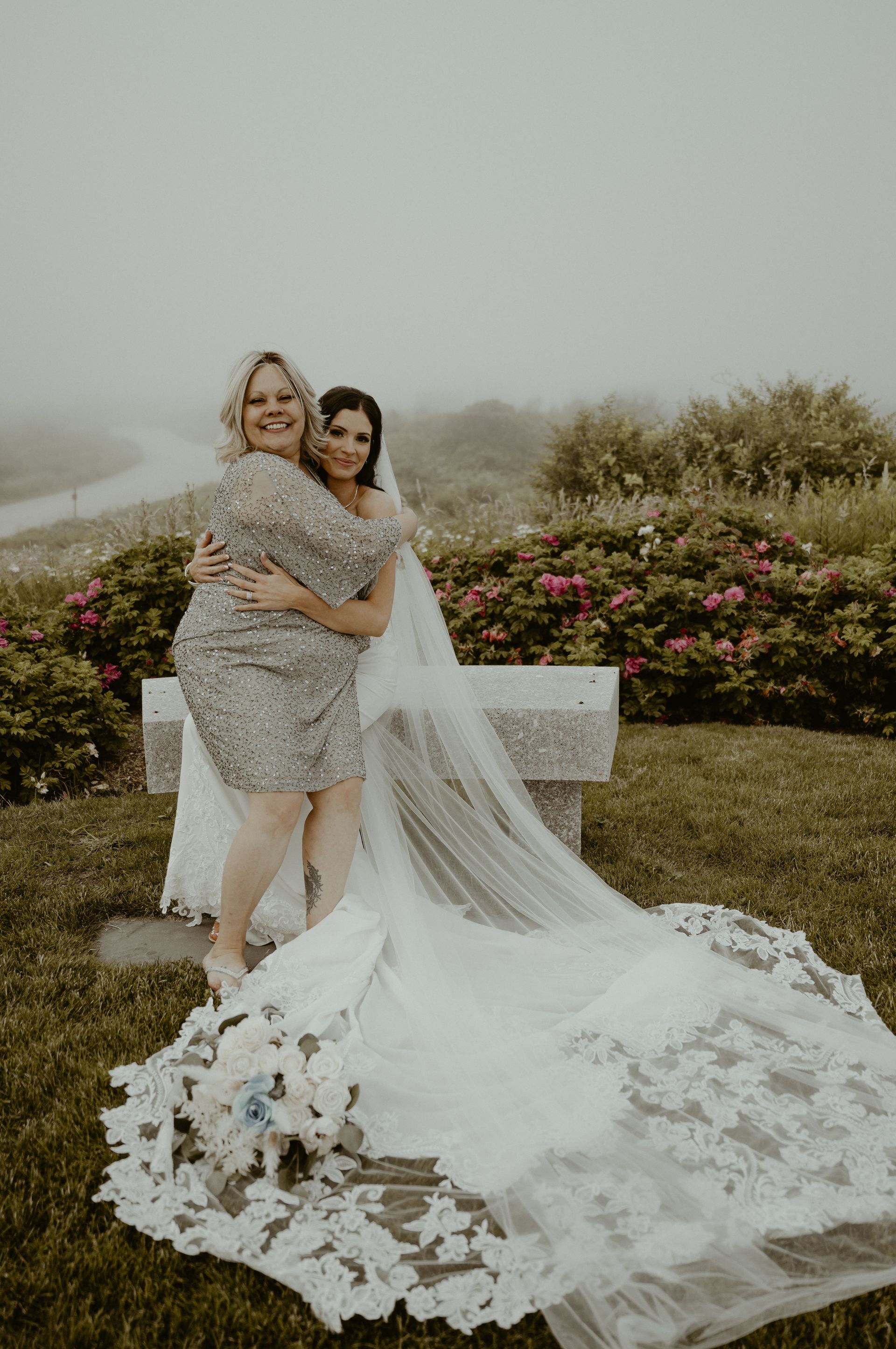 A mother of the bride is hugging her daughter in a wedding dress.