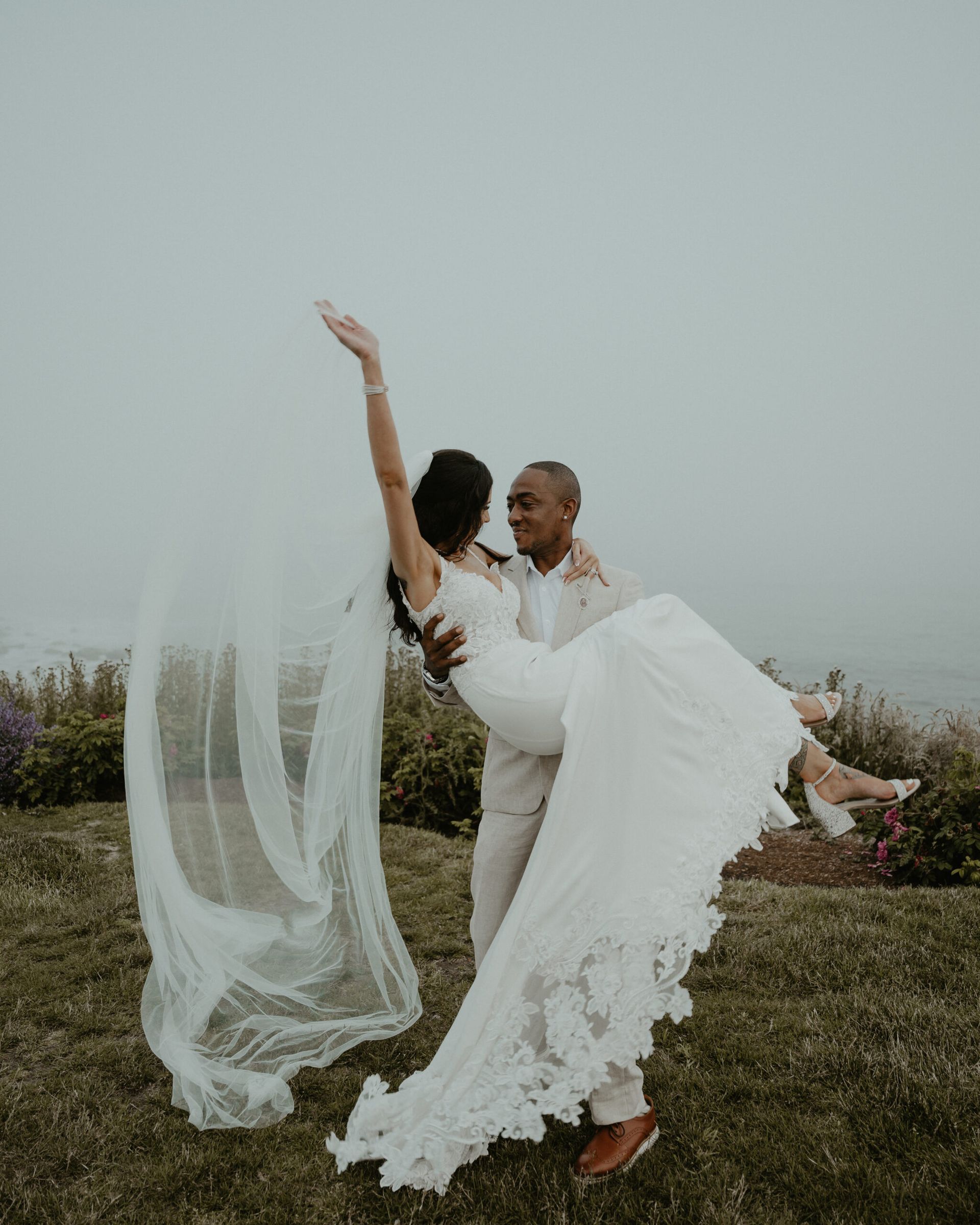A man is holding a bride in his arms in a field.