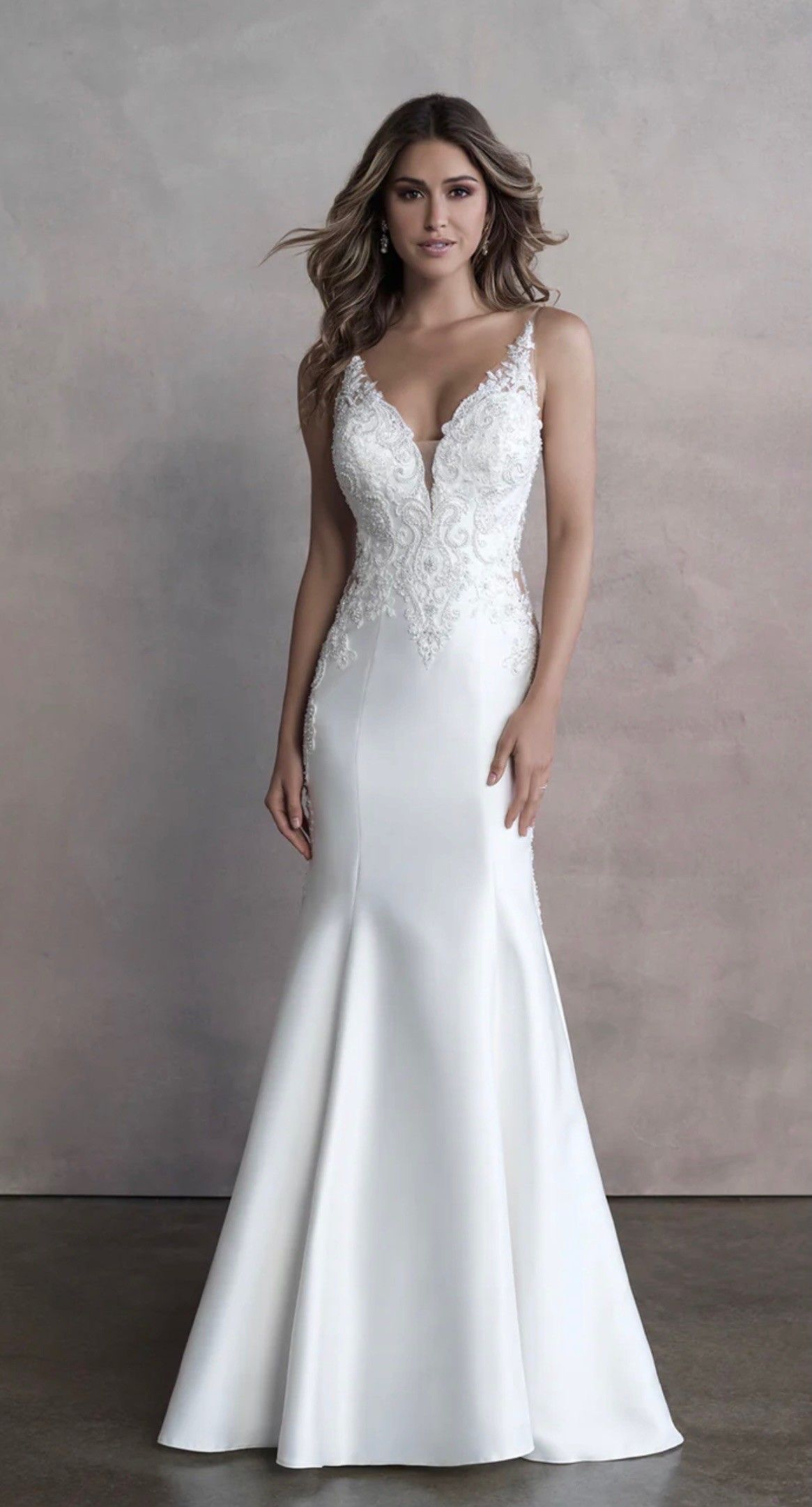 A model wearing a white, V-neck, floor-length mermaid wedding dress with lace embroidery on the bodice.