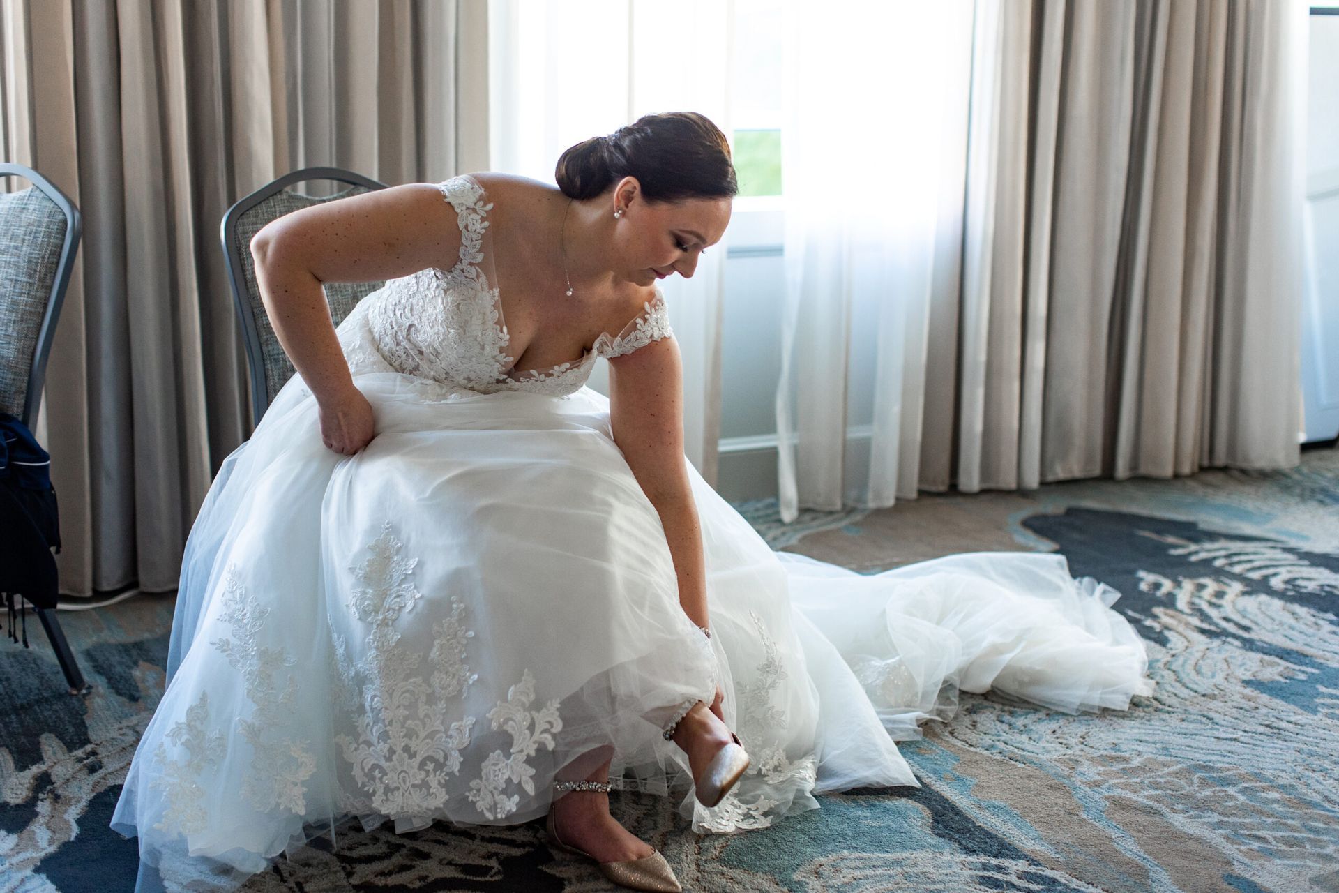 A bride is sitting on a chair putting on her wedding shoes.