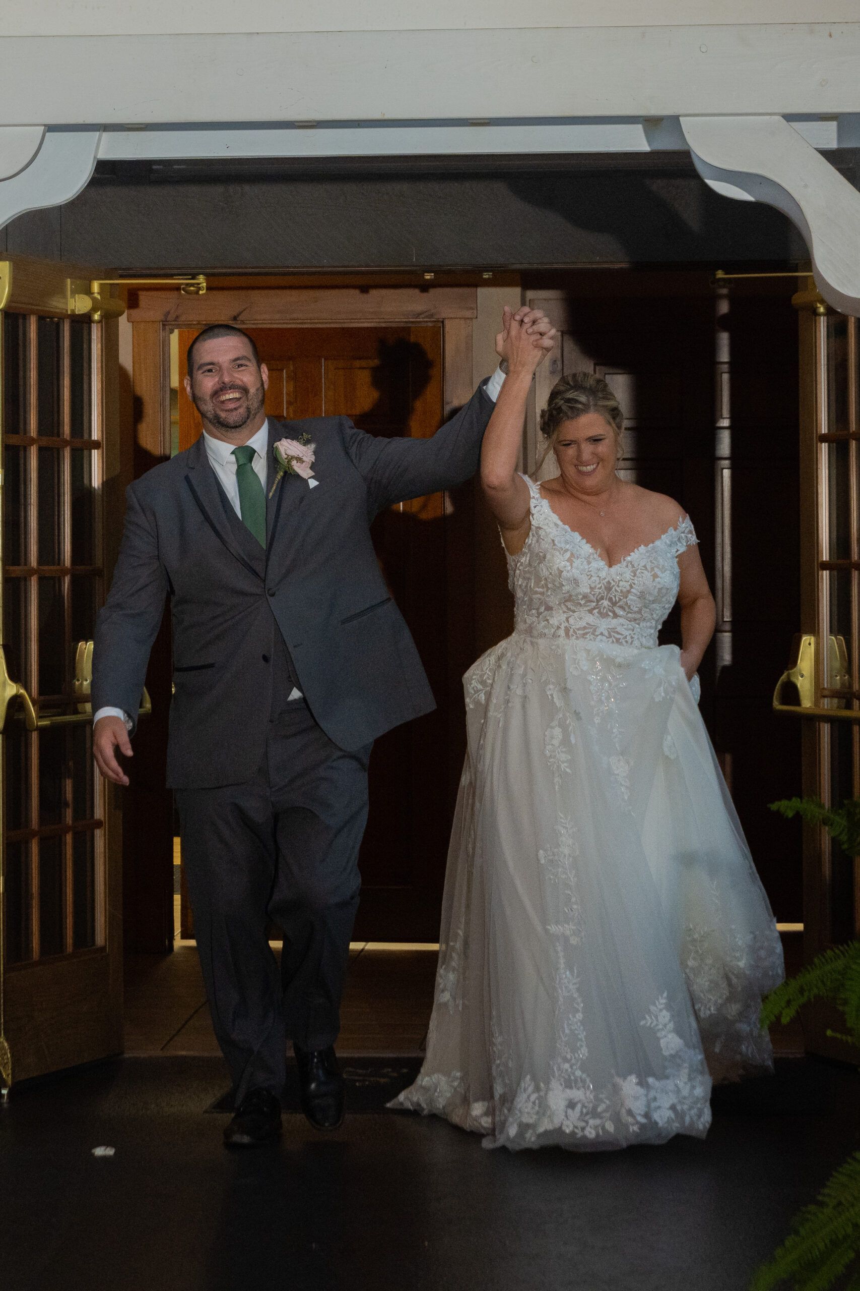 A bride and groom are walking out of a building with their arms in the air.