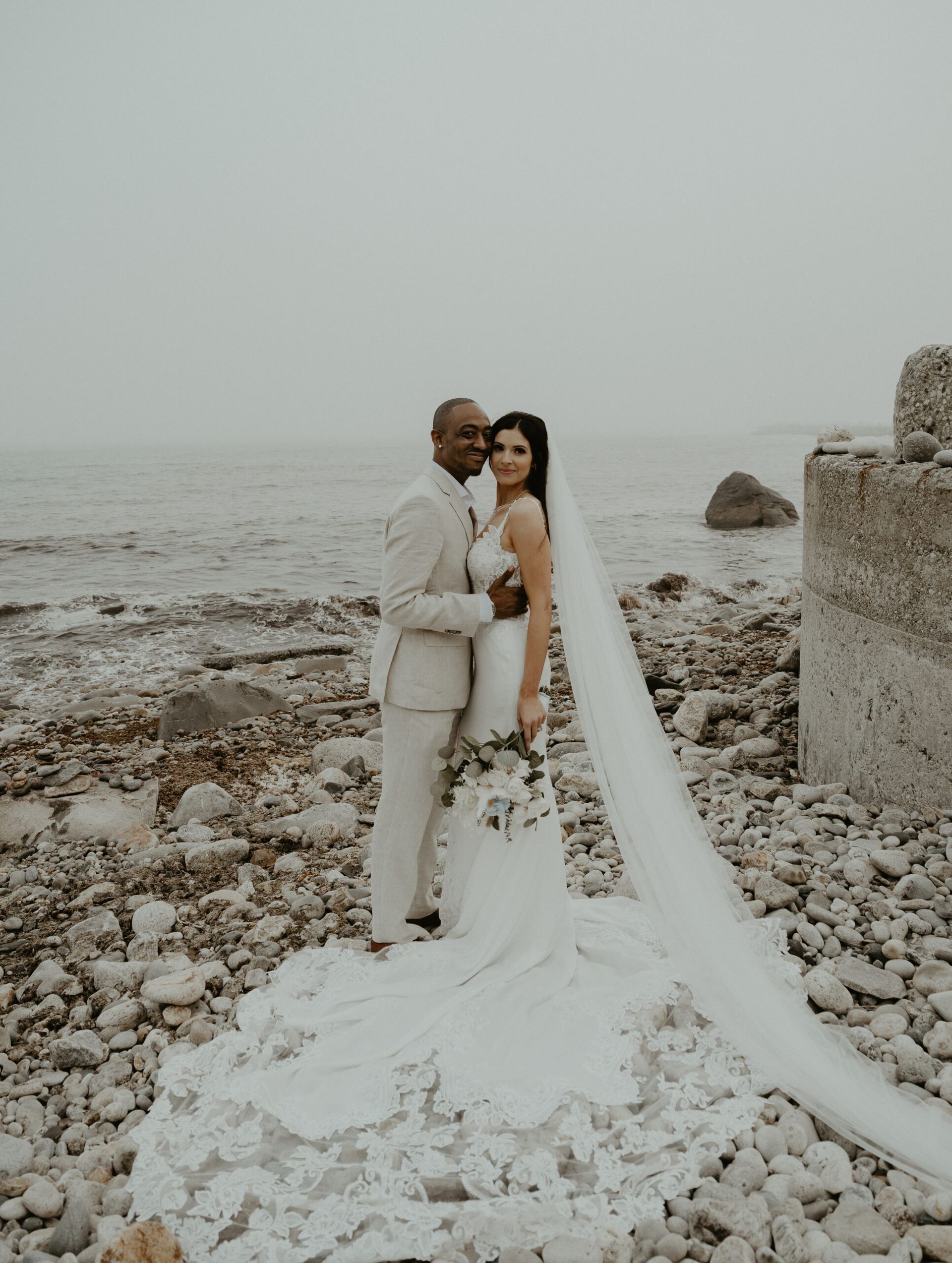 A bride and groom are posing for a picture on the beach.