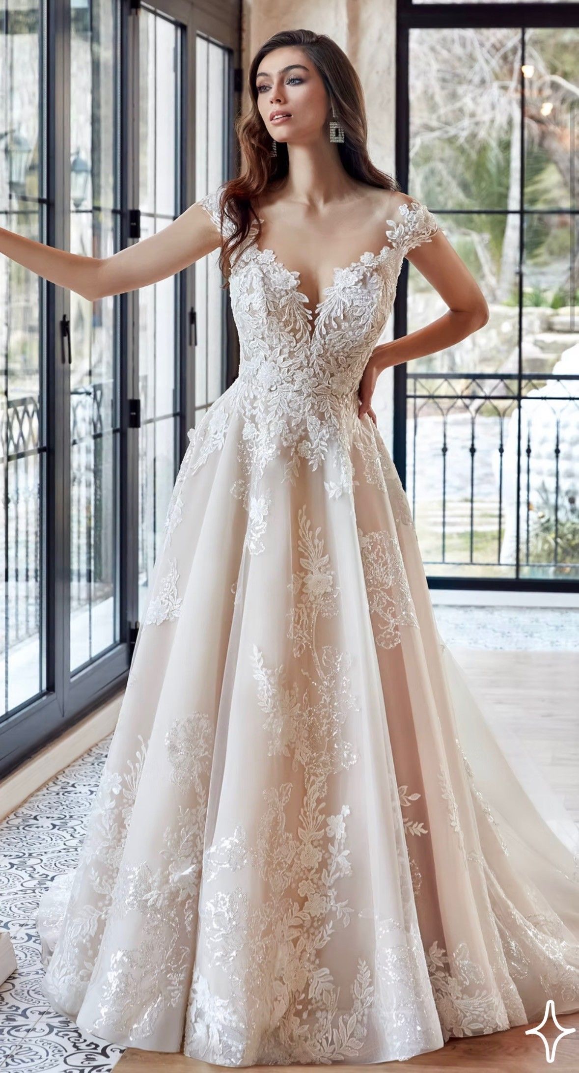 A model posing in a white, floral-embroidered A-line wedding gown with a plunging neckline and sheer bodice.