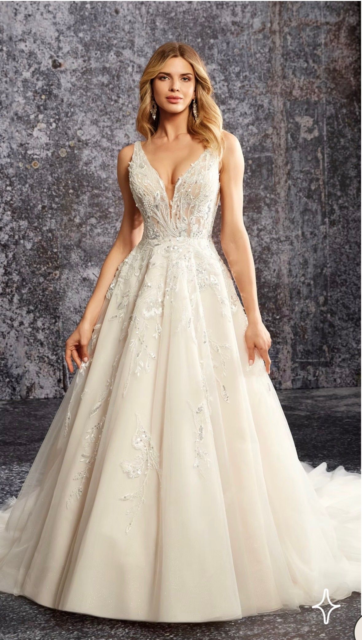 A model wearing an ivory A-line wedding dress with a deep V-neck, floral lace bodice, and a full tulle skirt.