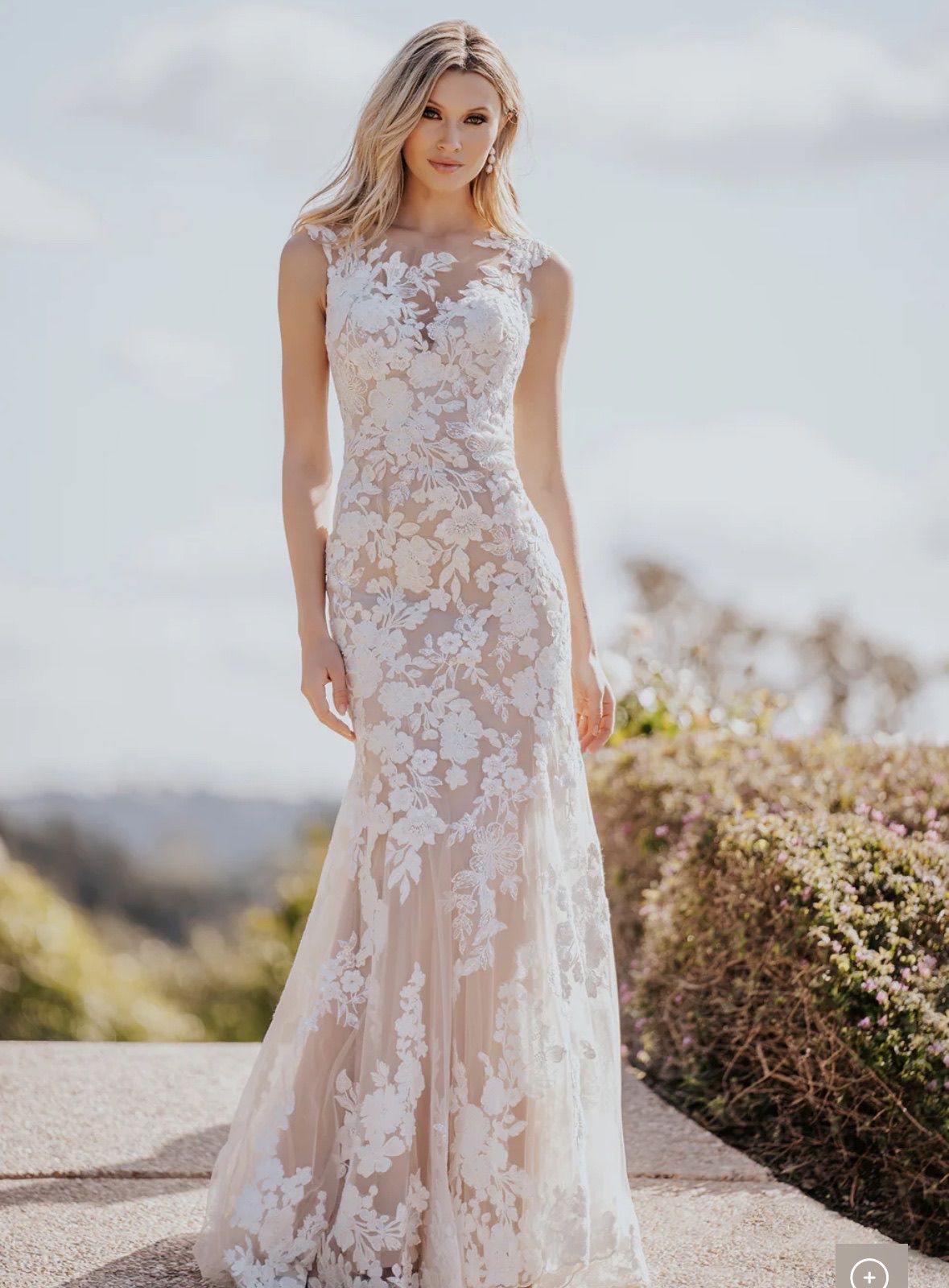 Blonde woman in a white lace wedding dress poses outdoors.