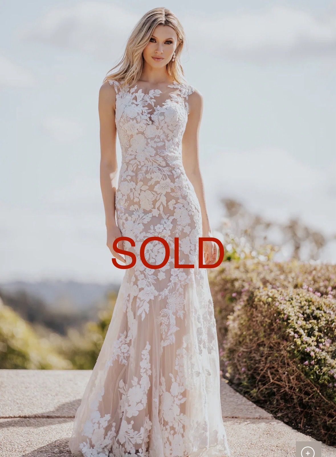 Blonde woman in a white lace wedding dress poses outdoors.