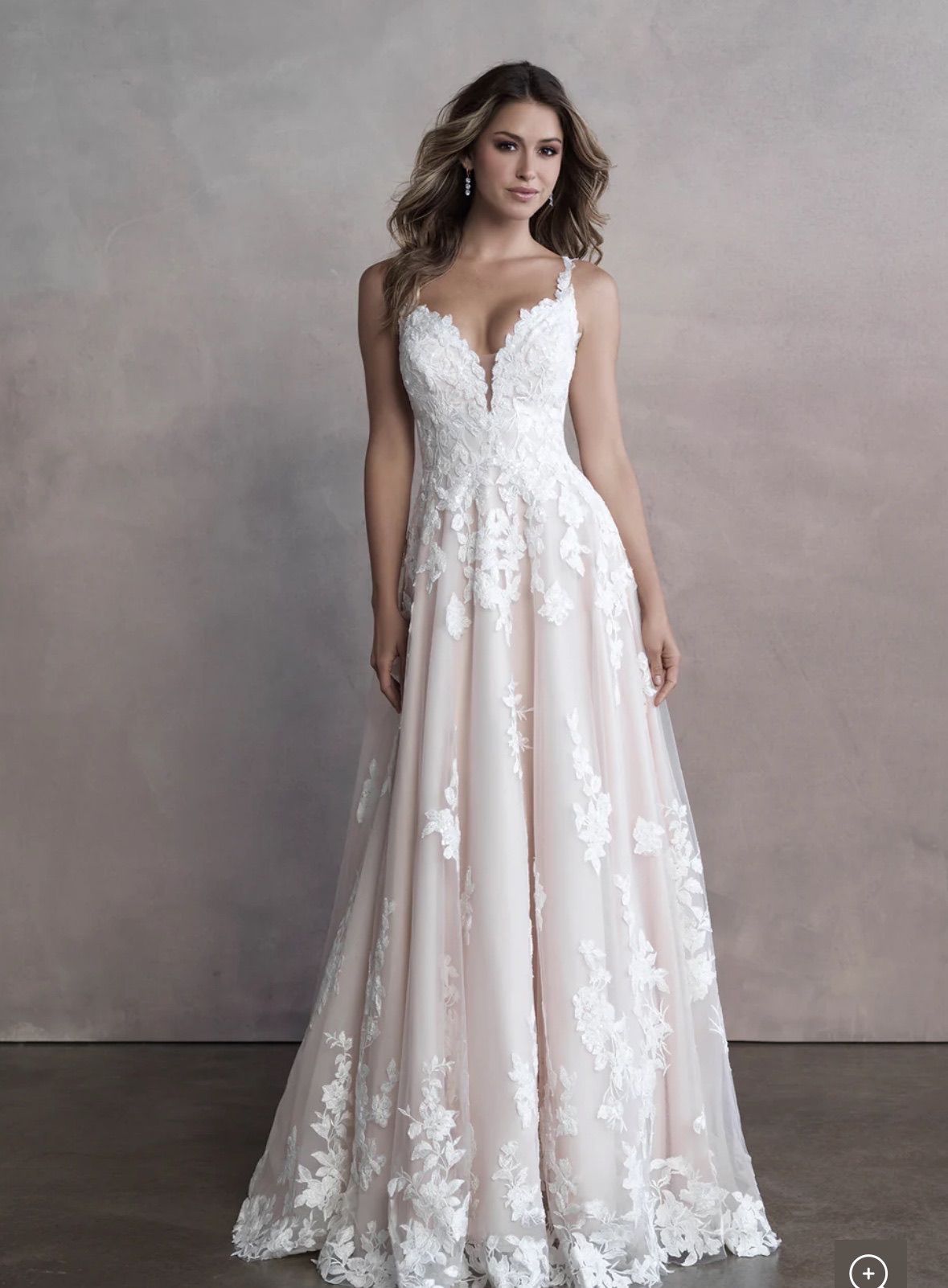 Woman in a white wedding dress with lace detail, standing in a studio with a neutral background.