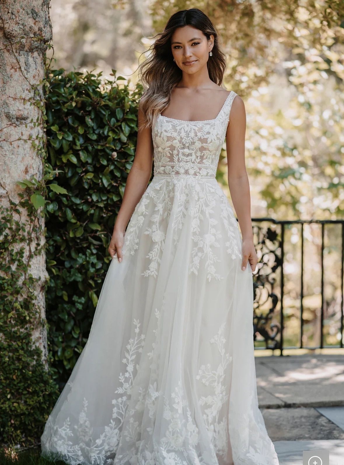 Woman in a white wedding dress with lace details, standing outdoors.
