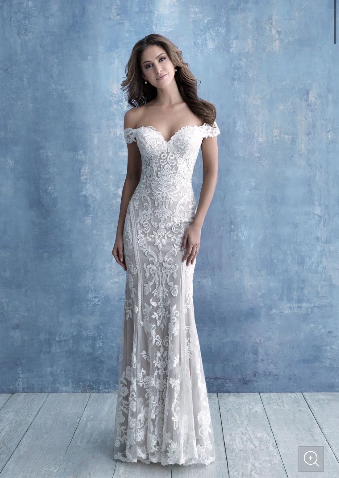 Woman in an off-shoulder white lace wedding dress, posing in front of a blue textured wall.