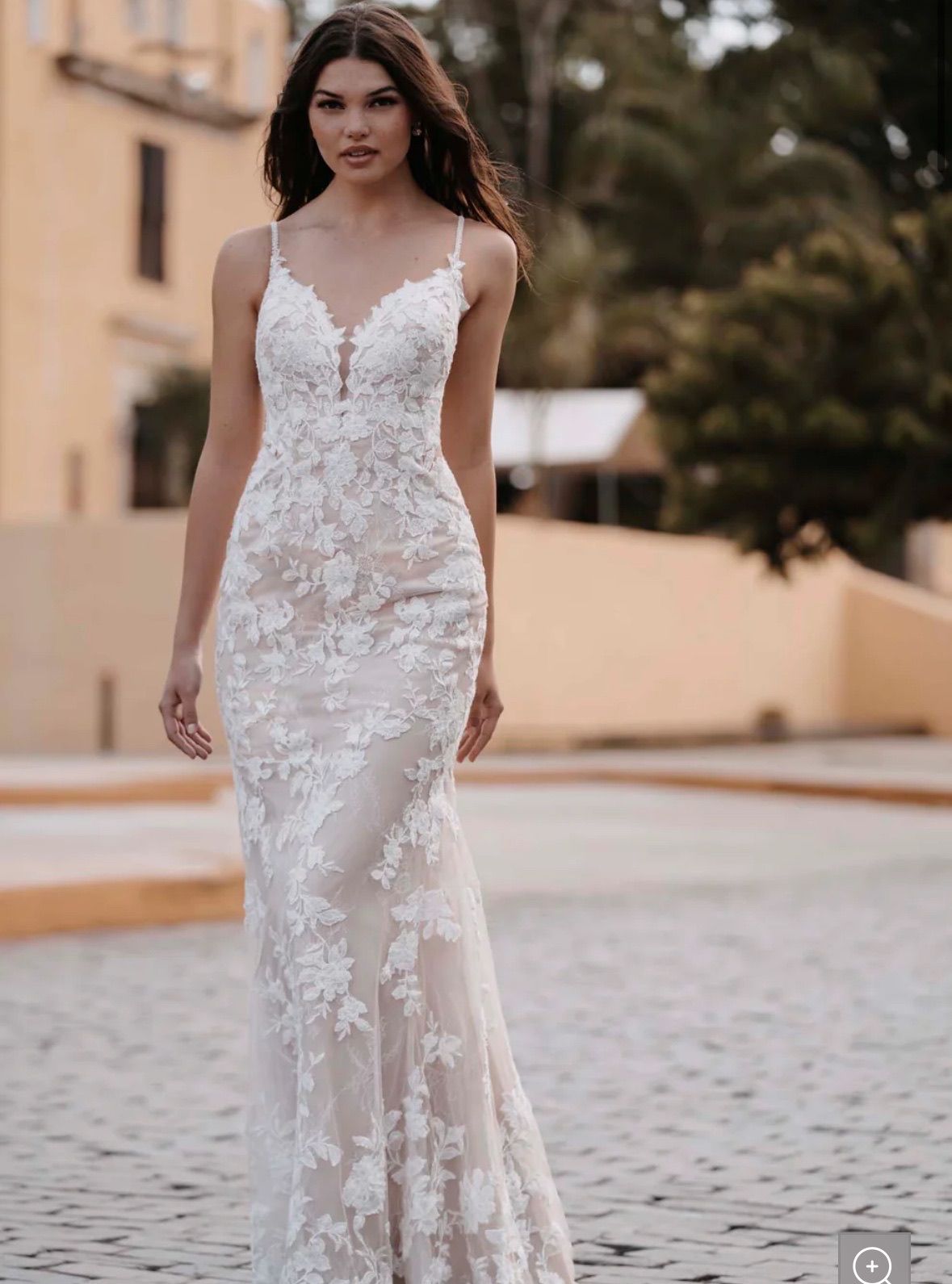 Woman in a white lace wedding dress with spaghetti straps walks on cobblestone street.