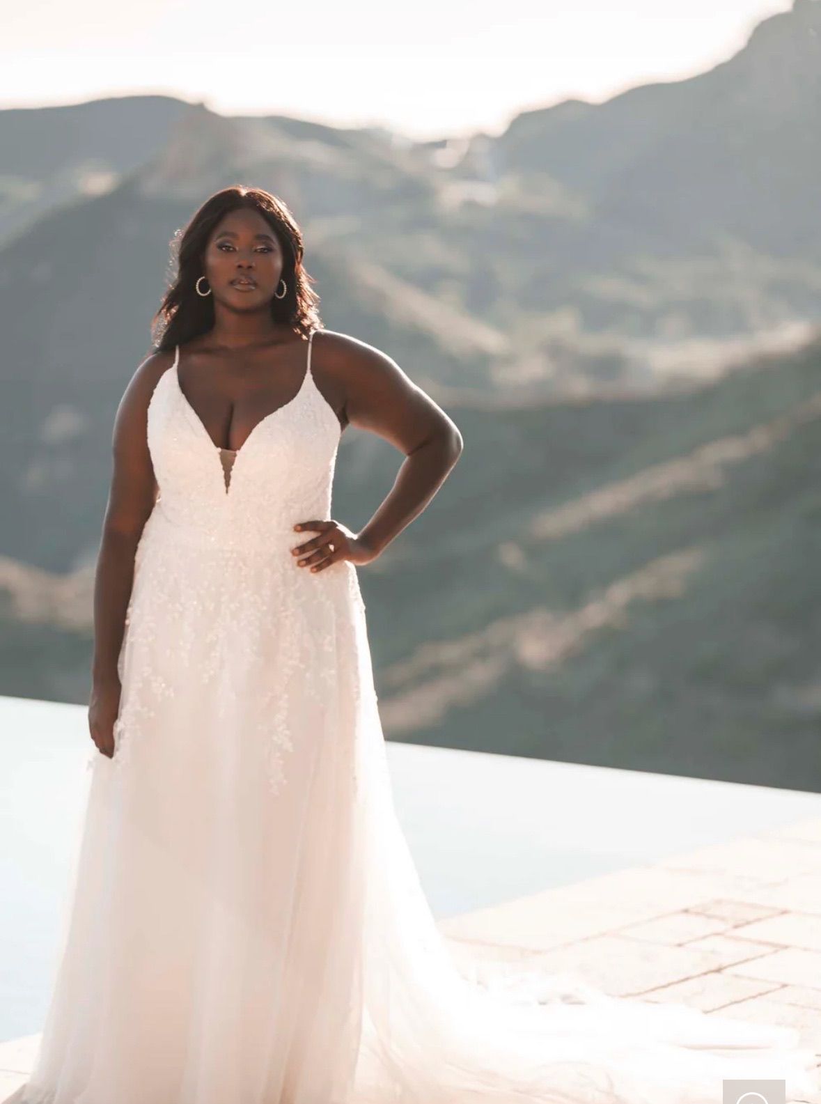 Woman in white wedding dress with a plunging neckline, posing outside with mountain backdrop.