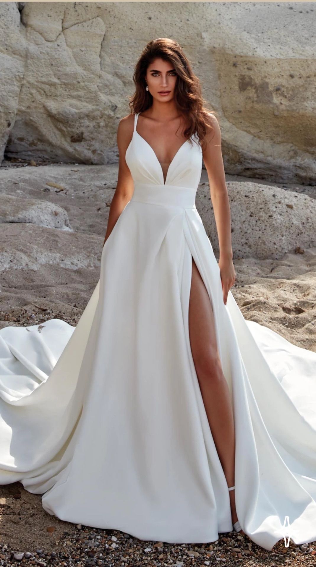 Woman in a white wedding dress with a thigh-high slit, posing on a beach.